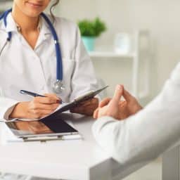A doctor sitting down and speaking with her patient in a clinical setting.