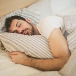 Man holding a pillow while sleeping in bed.