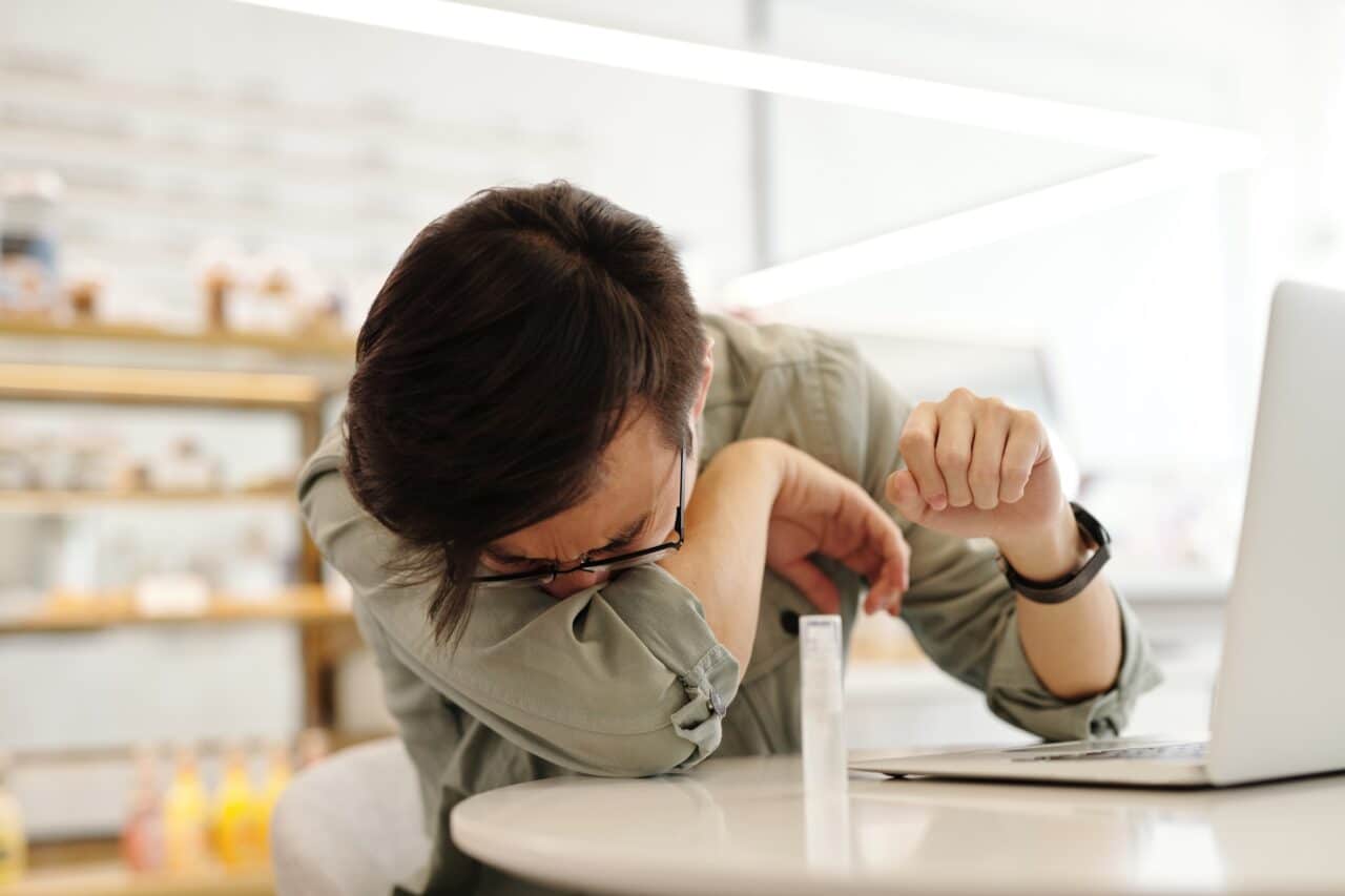 Man sneezing into his arm while out at a cafe.