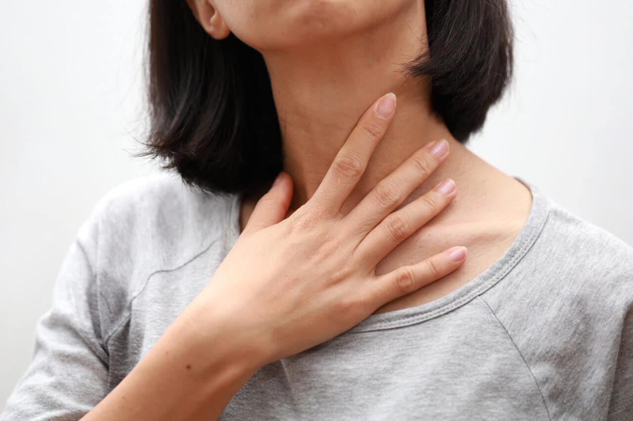 Closeup of woman touching her sore throat.