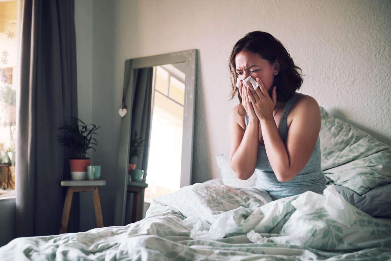 Woman blowing her nose while sick in bed.