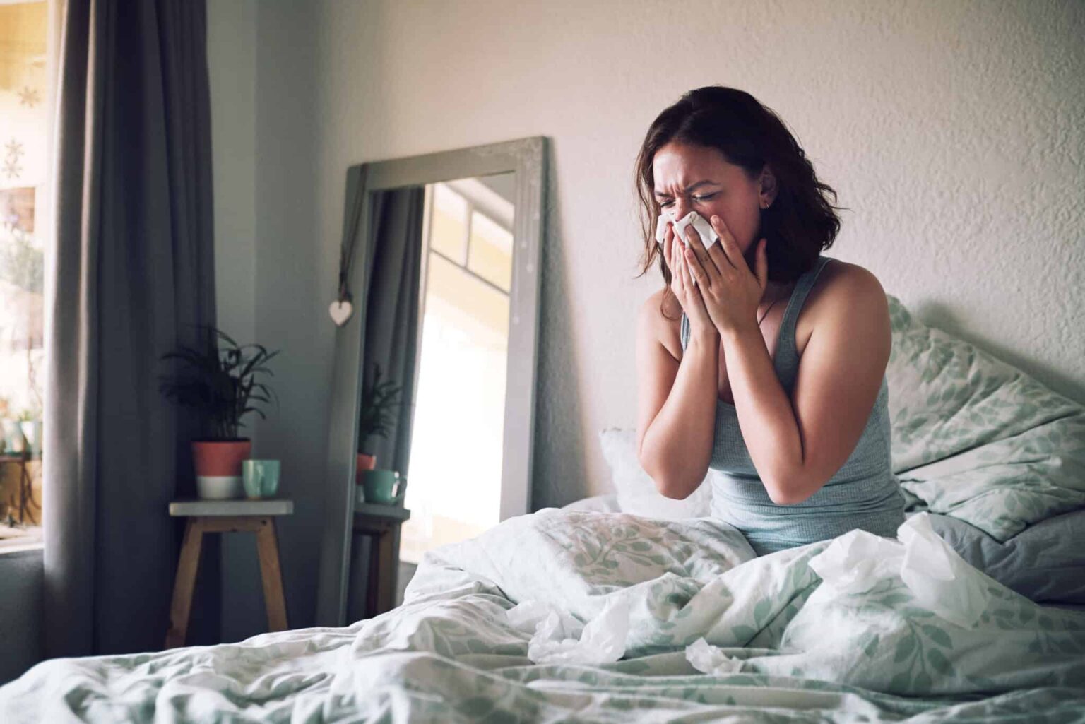 Woman blowing her nose while sick in bed.