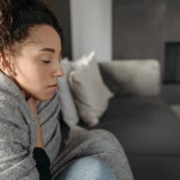 Woman sick at home, wrapped in a blanket on the couch.