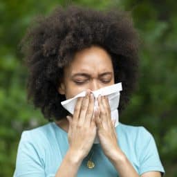 Woman with Sinusitis Problems is Feeling Displeased and Blowing Nose in Napkin During a Walk in City Park During a Summer Day.