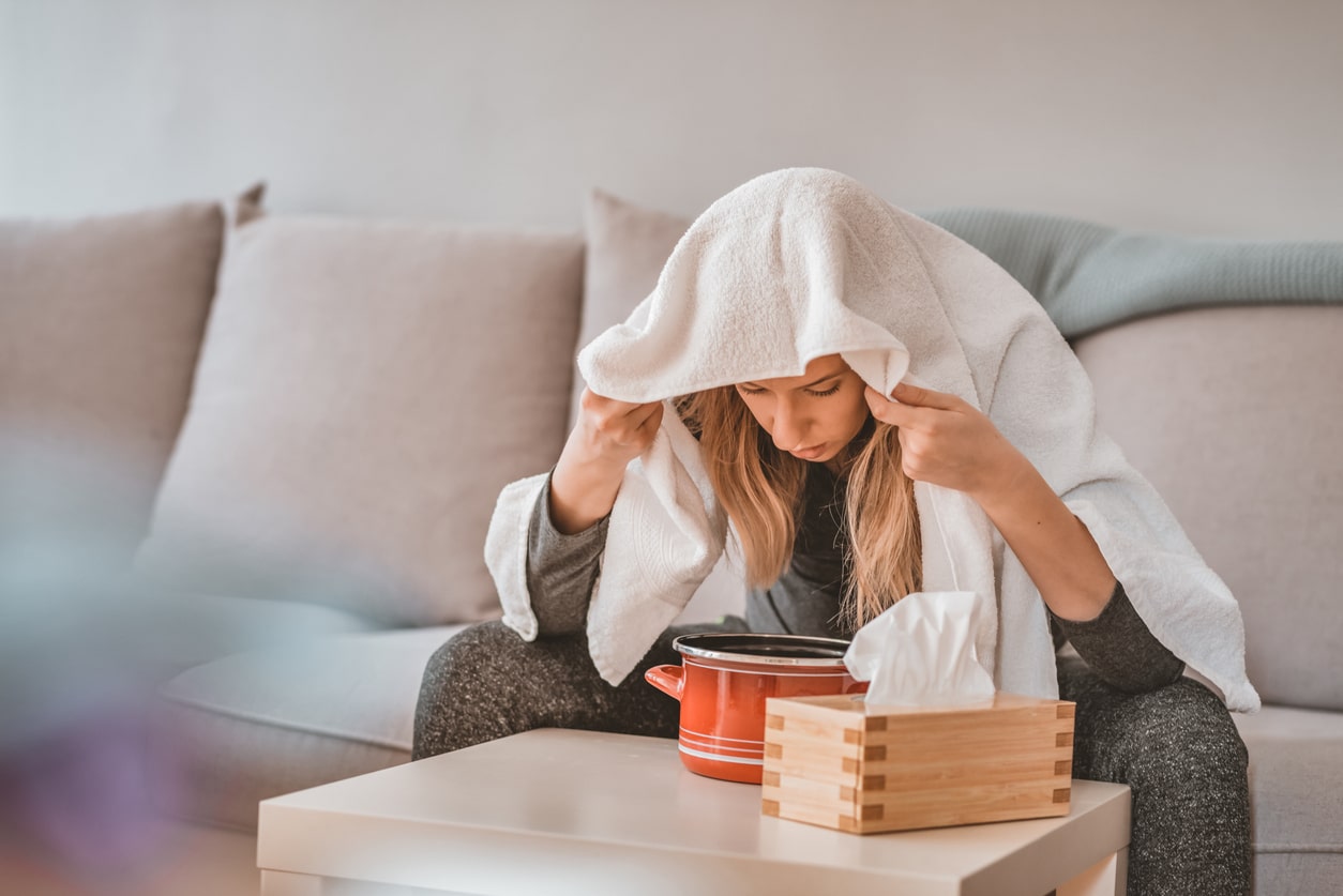 Sick woman sitting over a bowl of hot water to steam sinuses.