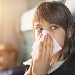 Young girl blowing her nose into a tissue on a train.