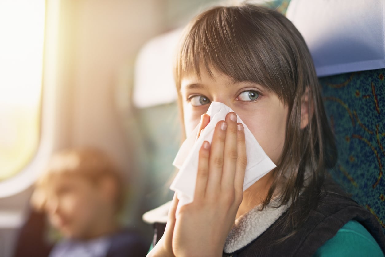 Young girl blowing her nose into a tissue on a train.