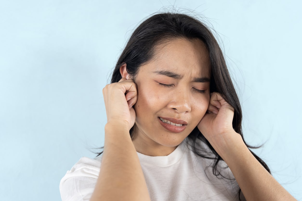Woman on blue background holding her ears.