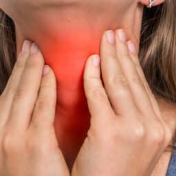 Woman with throat sore is holding her aching throat
