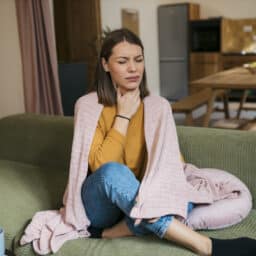Woman suffering from sore throat sitting on sofa