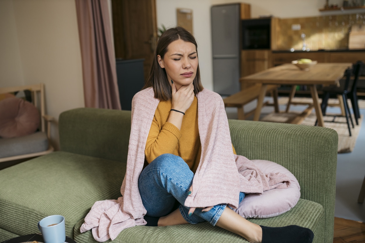 Woman suffering from sore throat sitting on sofa.