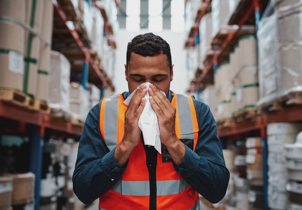Warehouse worker sneezing into a tissue