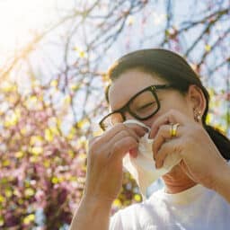 Woman with seasonal allergy using paper tissue to blow her nose