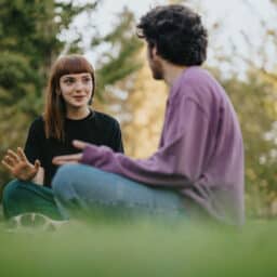Young friends sitting on grass, enjoying conversation outdoors in bright sunlight