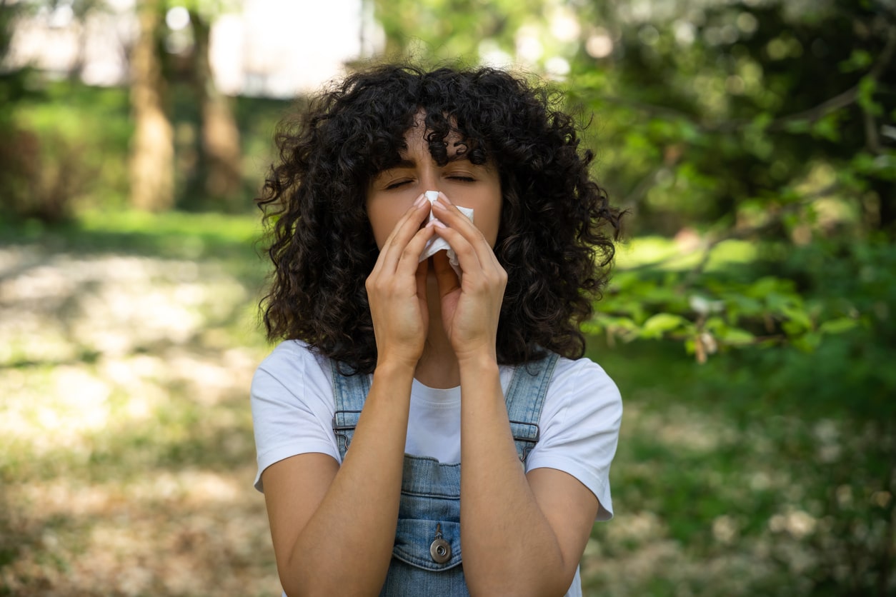 Woman with allergies standing outside, blowing her nose into a tissue.