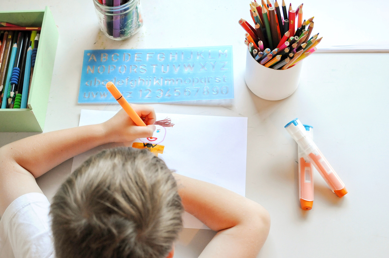 Child drawing at his desk with a couple of EpiPens next to him.