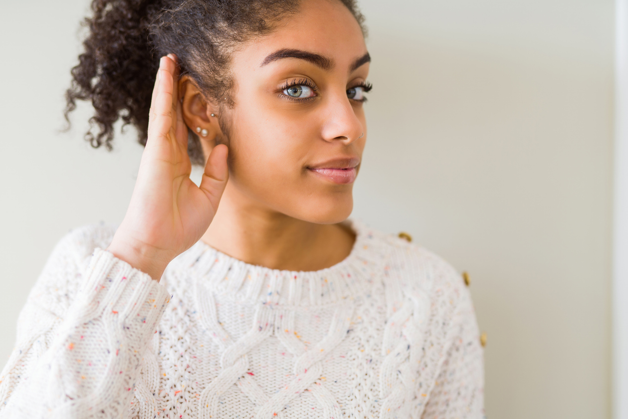 Young woman holding her hand to her ear.
